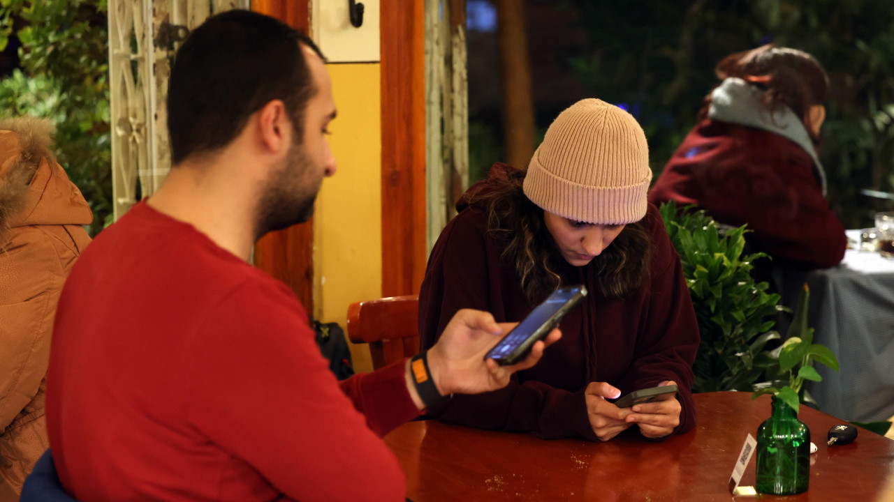 muškarac i žena gledaju u telefone dok sede u kafiću