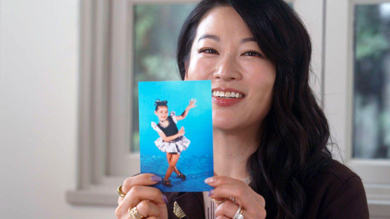 Headshot of Arden Cho smiling holding a childhood photo