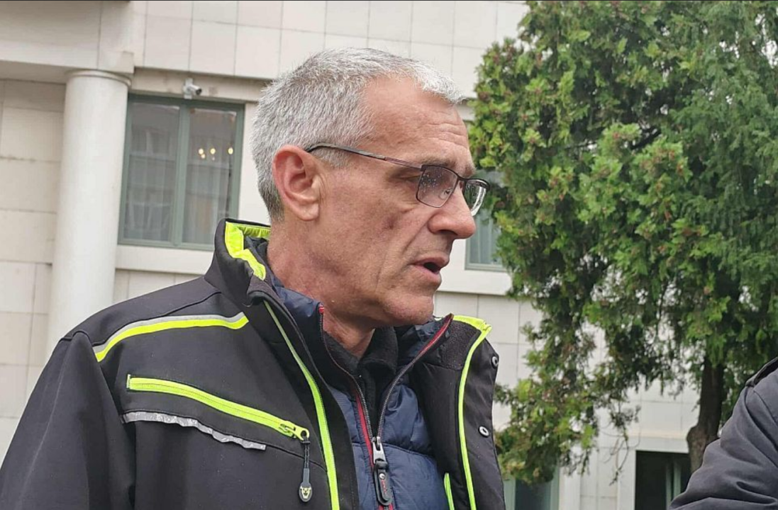 Sedi muškarac u tamnoj jakni sa svetlo zelenim detaljima gleda u stranu