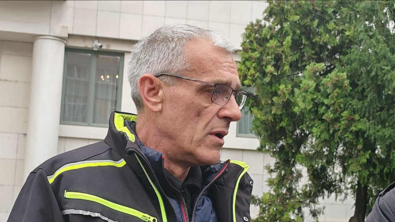 Sedi muškarac u tamnoj jakni sa svetlo zelenim detaljima gleda u stranu