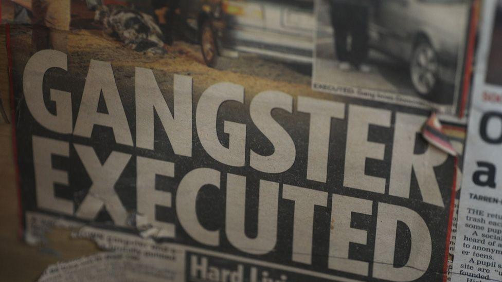 Isečak iz novina zakačen za zid kancelarije pastora Engela podsetnik je na ubistvo jednog od ozloglašenih vođa bandi 2019. godine