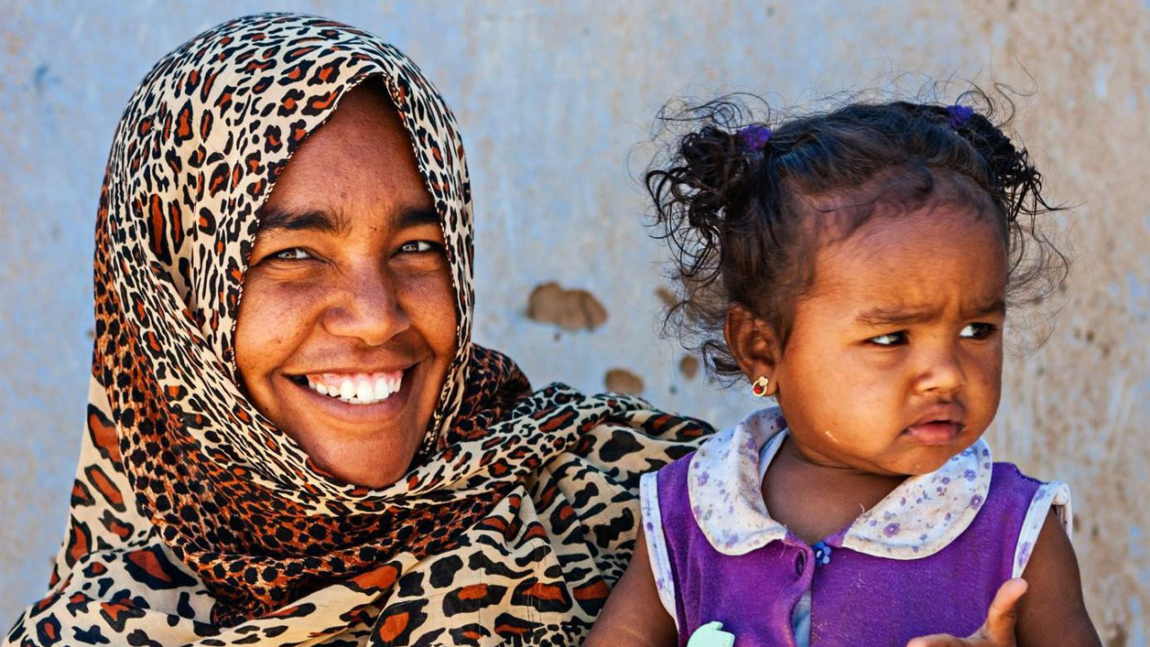 Severnoafrikanka se osehuje dok u rukama drži dete obučeno u roze haljinicu 