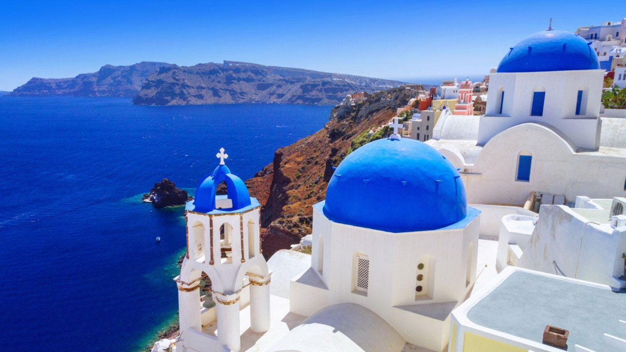 The town of Oia in Santorini, with white buildings and vibrant blue dome roofs and an amazing blue ocean