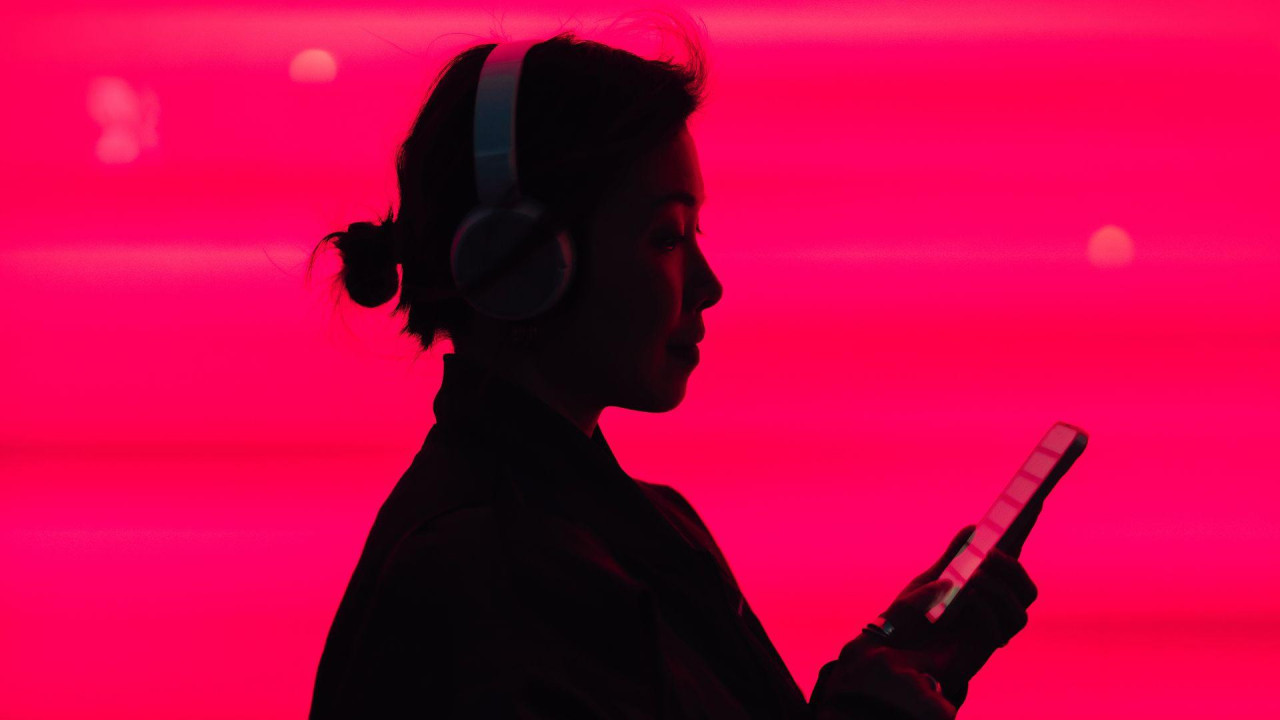 Woman in silhouette listening to music on smarphone in front of a bright pink background