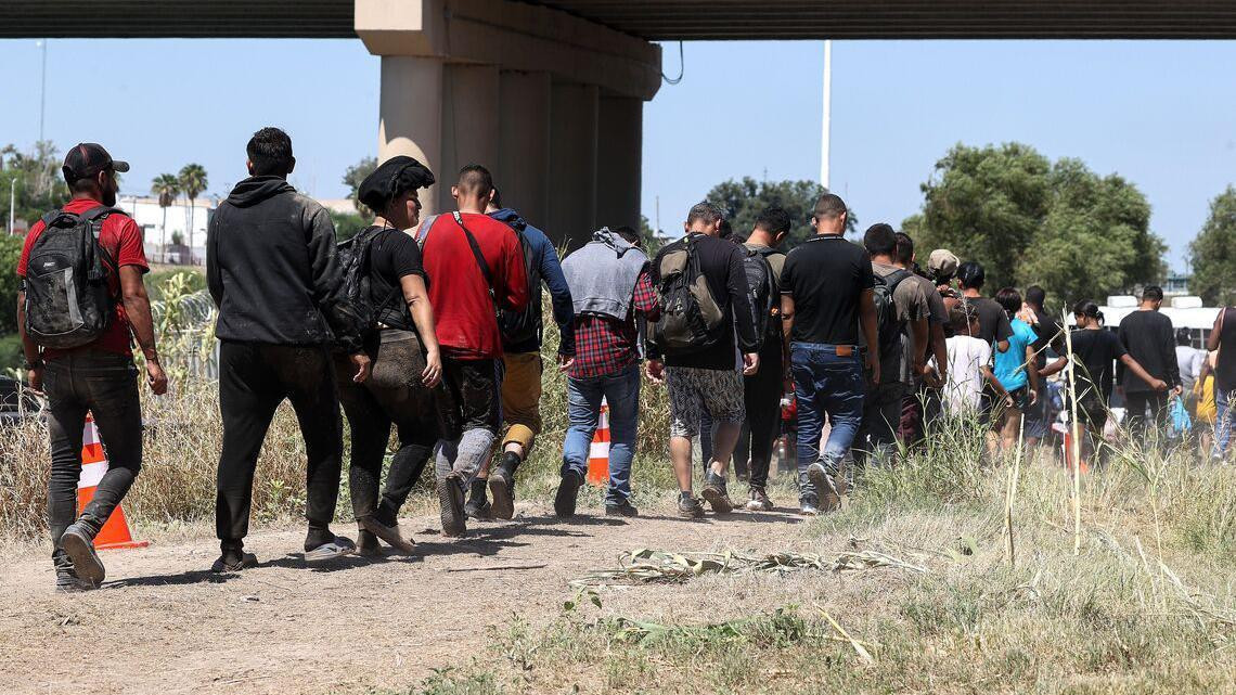 Kolona ljudi, mahom muškaraca prolazi ispod mosta 