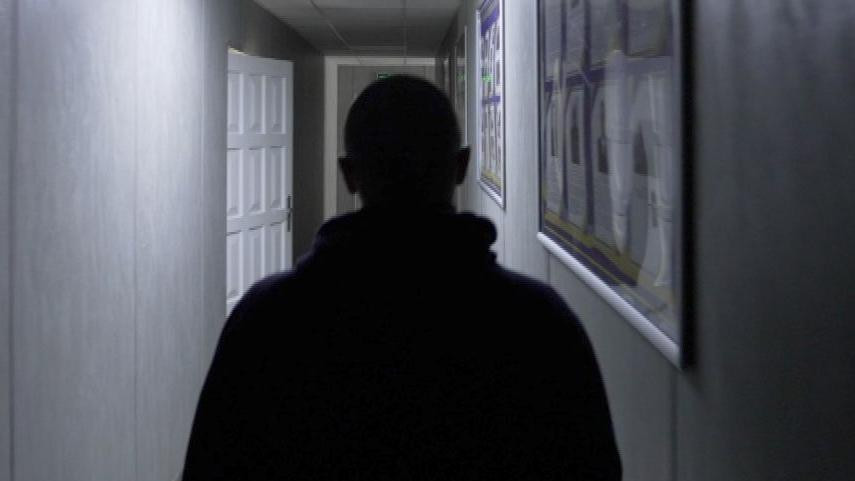 A rear view of the top half of Vlad in silhouette in a poorly-lit corridor of the Rivne detention centre. His head is shaven.