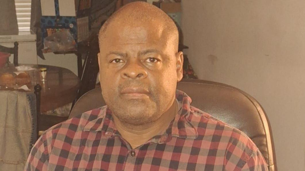 Ron Bishop sitting with a plaid shirt, hands crossed and looking at the camera.