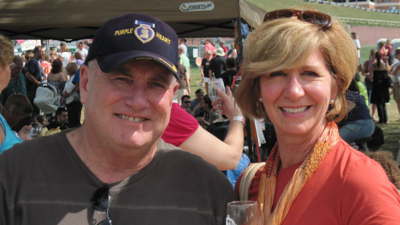 muškarac i žena gledaju i kameru i smeše se, žena sa čašom u ruci