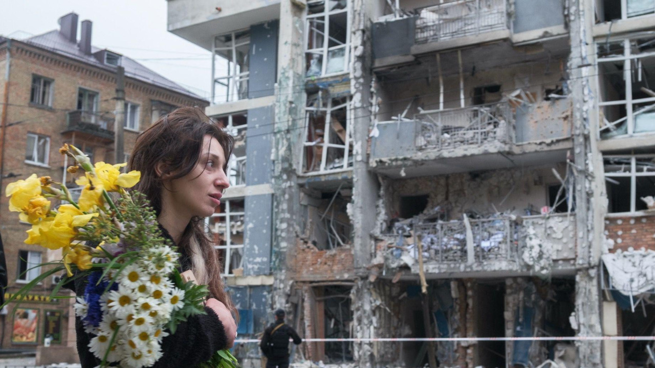 
                    Žena sa buketom cveća prolazi pored stambene zgrade u Ševčenkivskom okrugu Kijeva 25. maja 2025. Kosa joj je raščupana. Višespratna zgrada teško je oštećena u napadu ru