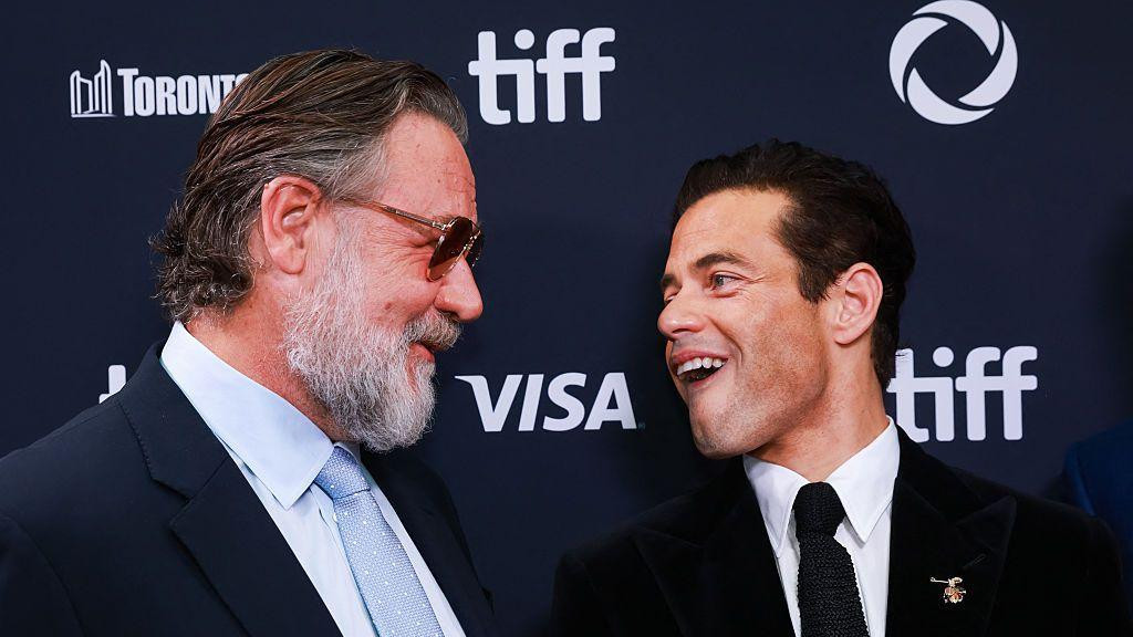 Glumci Rasel Krou, sa tamnim naočarima, i Rami Malek se smeju - obojica u odelima i kravatama - zajedno na premijeri filma „Nirnberg“ u Kanadi, u septembru 2025. godine.