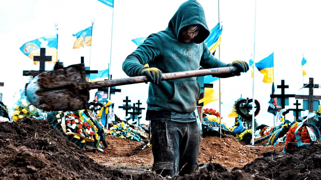 
                    Muškarac kopa grob na groblju u Odesi 16. marta 2024. Oko deset ukrajinskih zastava vijori se na belim jarbolima iza njih. Kopač groba u nosi tirkiznu duksericu sa kapulj