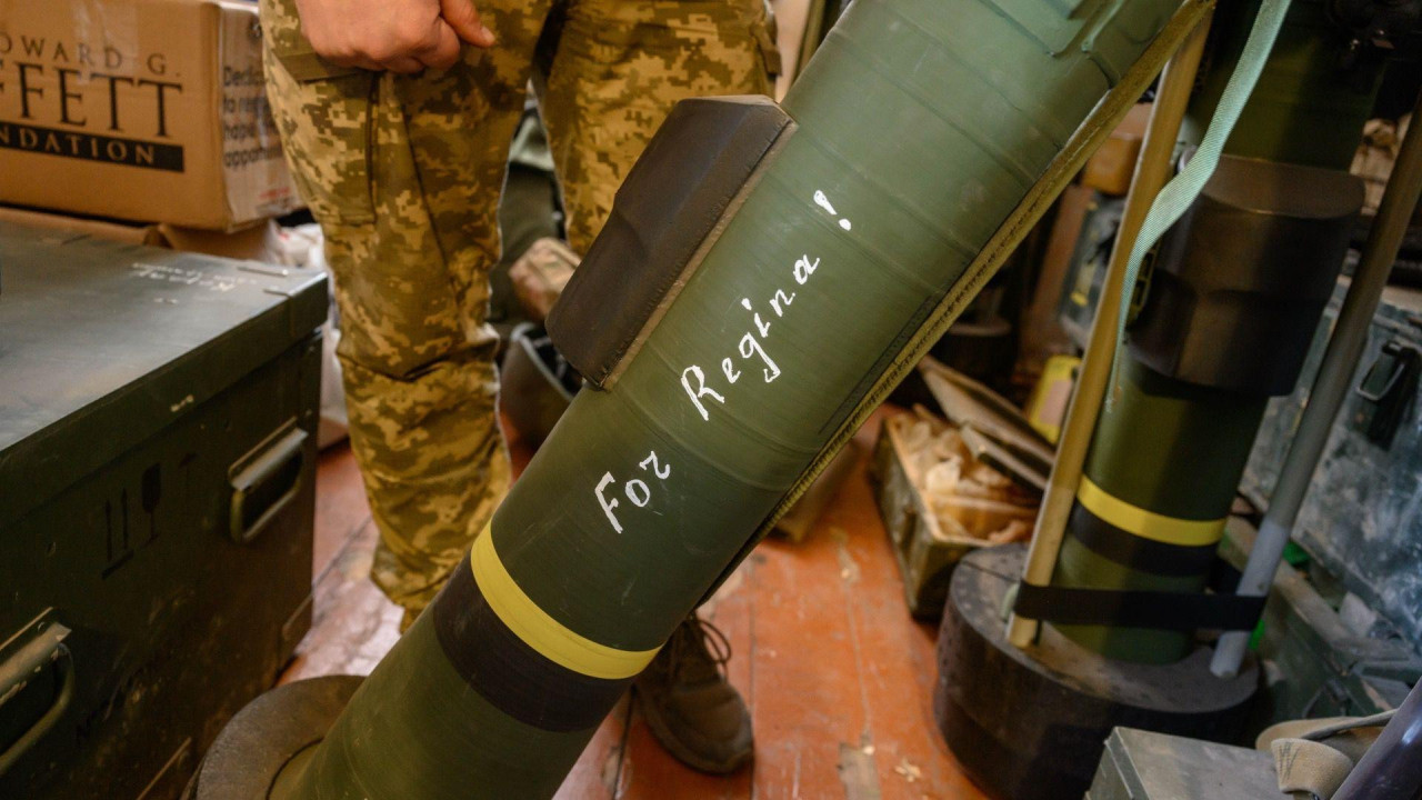 Zelena raketa sa natpisom „Za Reginu!“ belom bojom. Raketa je na postolju na podu unutar sobe, a iza nje su noge vojnika u kamuflažnim pantalonama. 