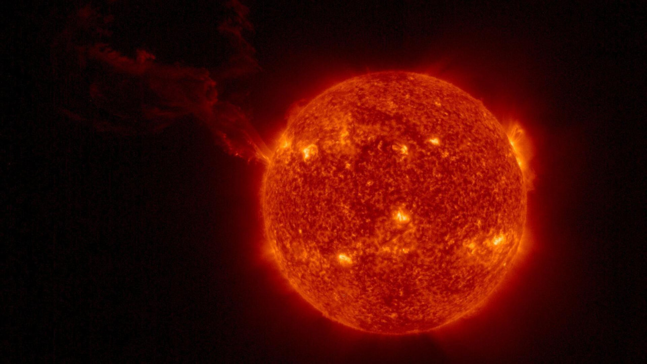 Sunce se vidi kao crvena lopta sa žutim tačkama na površini; dugačak oblak se proteže ulevo.