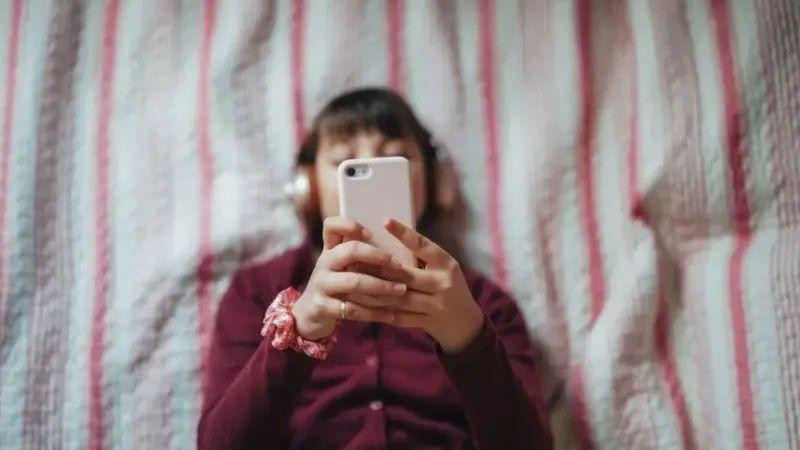 devojčica gleda u telefon dok leži na krevetu