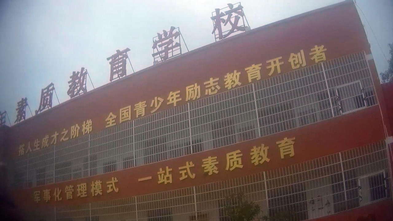 Image taken from undercover filming showing a dark red building with metal grilles covering open-air corridors and Chinese writing on the walls.