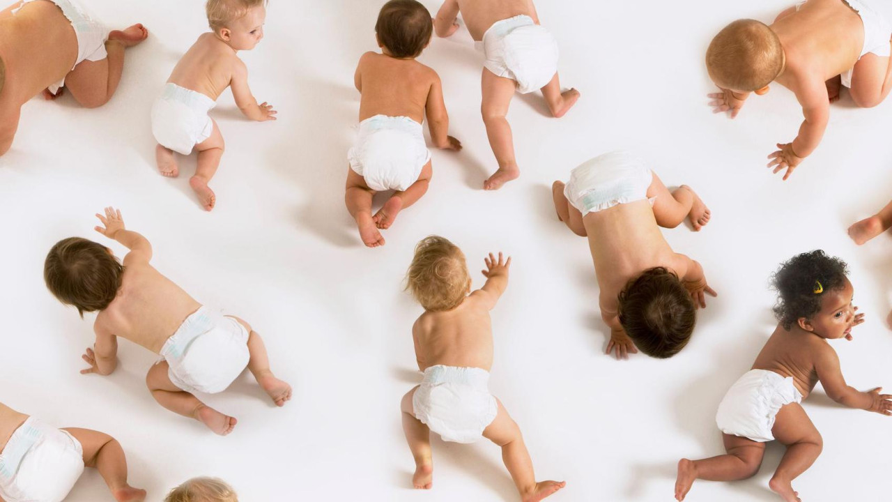 A group of babies wearing nappies crawling all over the floor in a white studio setting