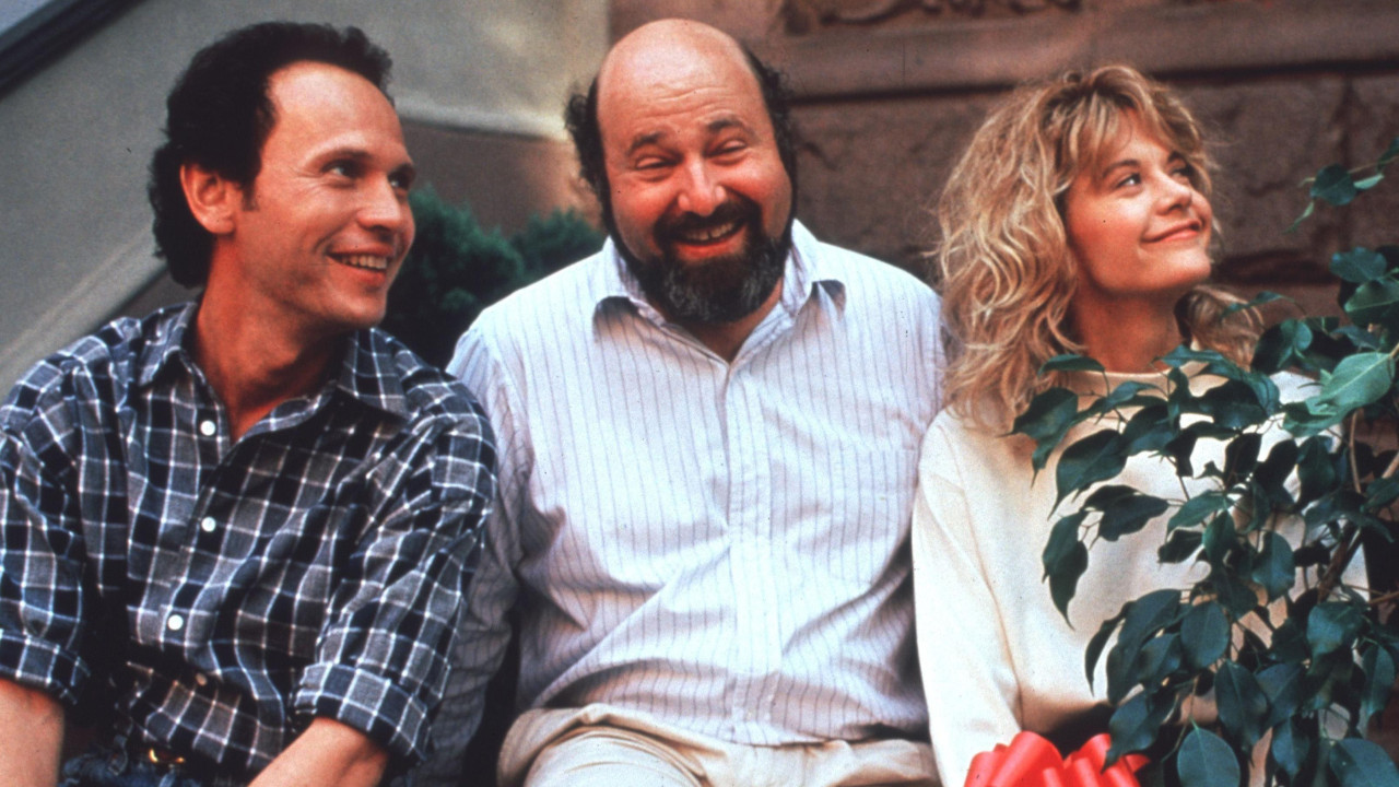 Billy Crystal, Rob Reiner and Meg Ryan sitting together on a step and smiling while filming When Harry Met Sally