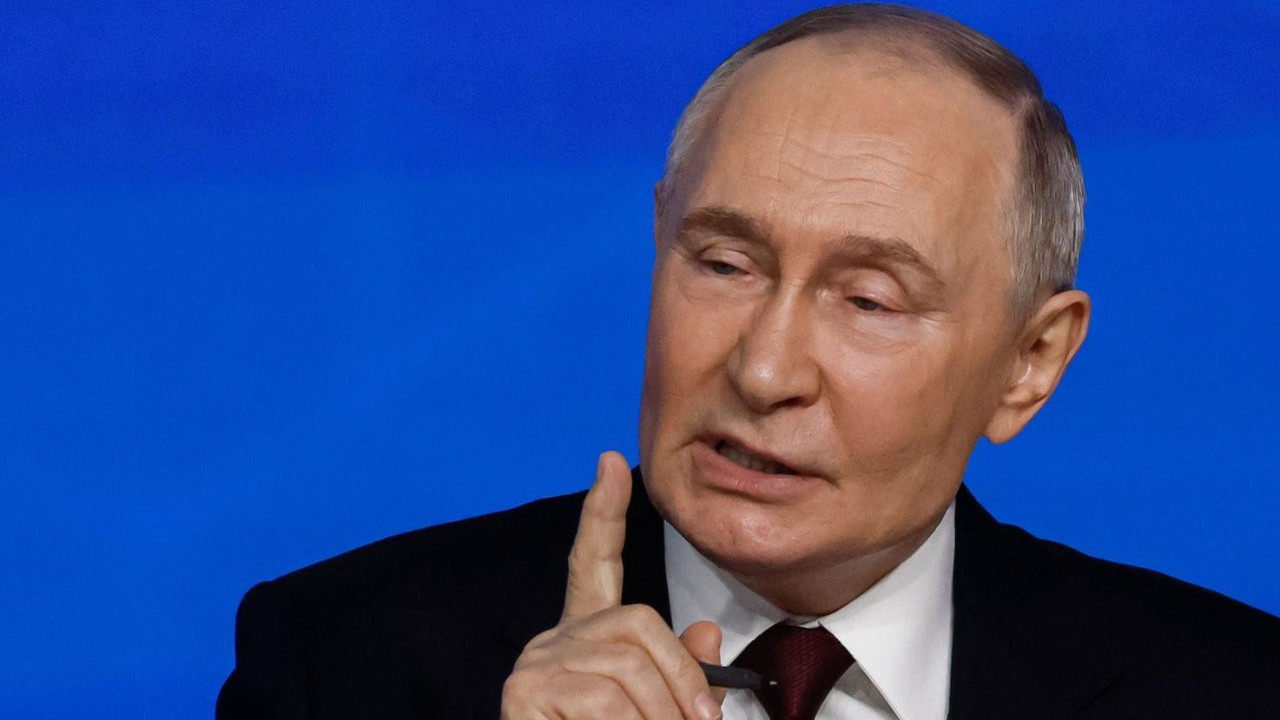 Putin pokazuje prstom u pravcu publike, u tamnom odelu i beloj košulji, talkinghead format