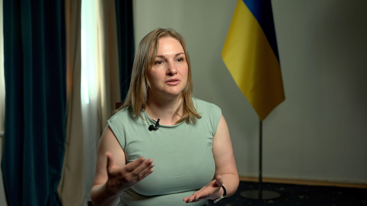 Žena u zelenoj majici iza nje se vidi ukrajinska zastava