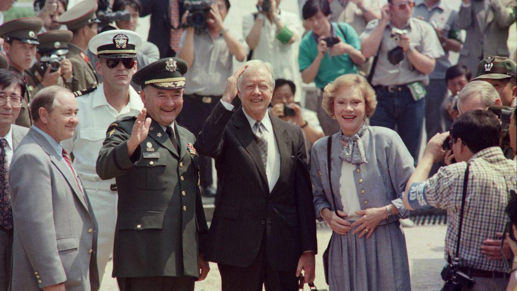 
                    Bivši predsednik SAD Džimi Karter, u crnom odelu sa sivom kravatom i u beloj košulji, sa suprugom Rozalin u sivom kompletu i beloj majici prelazi granicu i ulazi u Severn