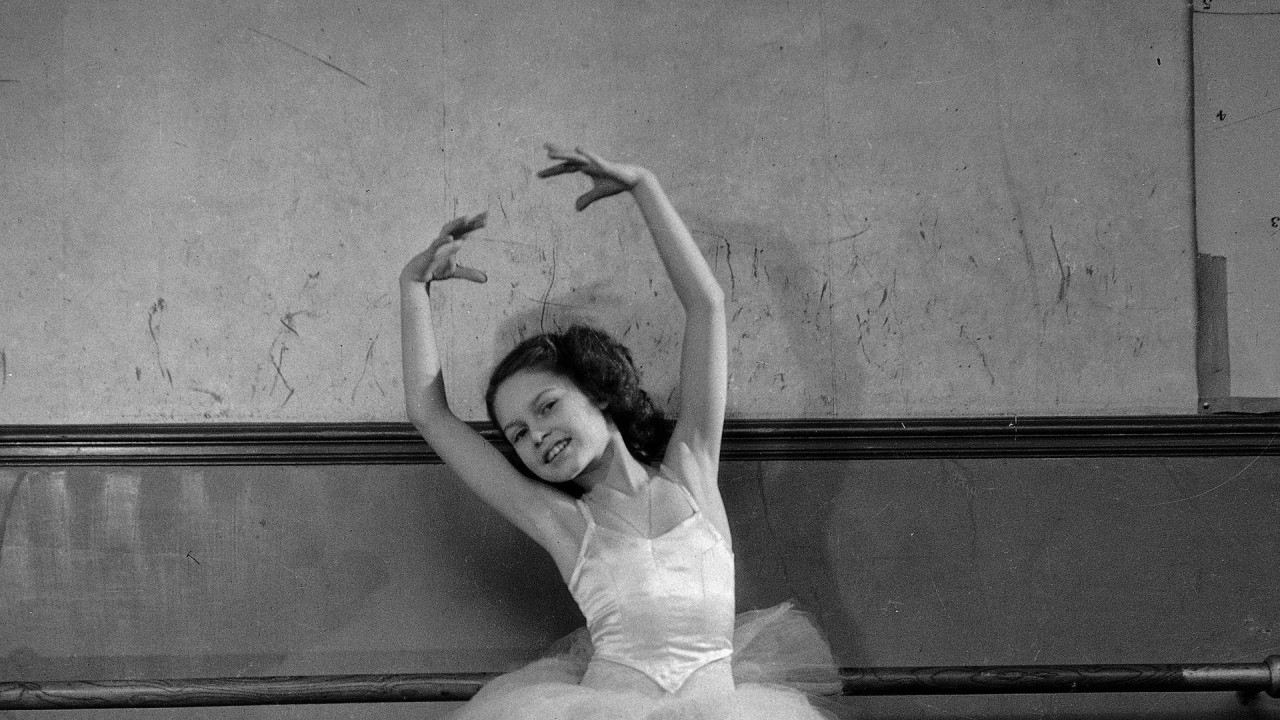 Na crno-beloj fotografiji iz 1946. godine, Brižit Bardo pozira u baletskoj haljini, stoji na prstima s podignutim rukama, blago nagnuta ulevo.