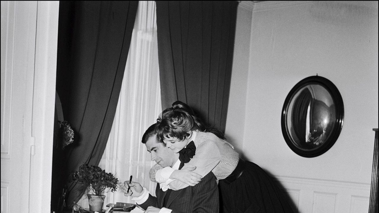 Brižit Bardo, u bluzi i dugoj crnoj suknji, grli Rožea Vadima dok on sedi za stolom i radi u njihovom domu 1952. godine.