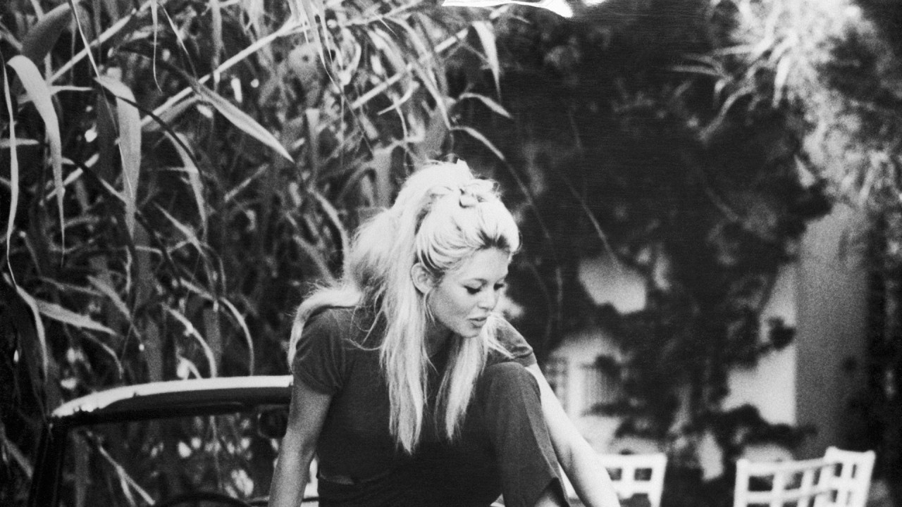 U svojoj vili u Sent Tropezu, Brižit sedi bosa na gepeku automobila, dok joj razigrani jazavičar skače ispred nje