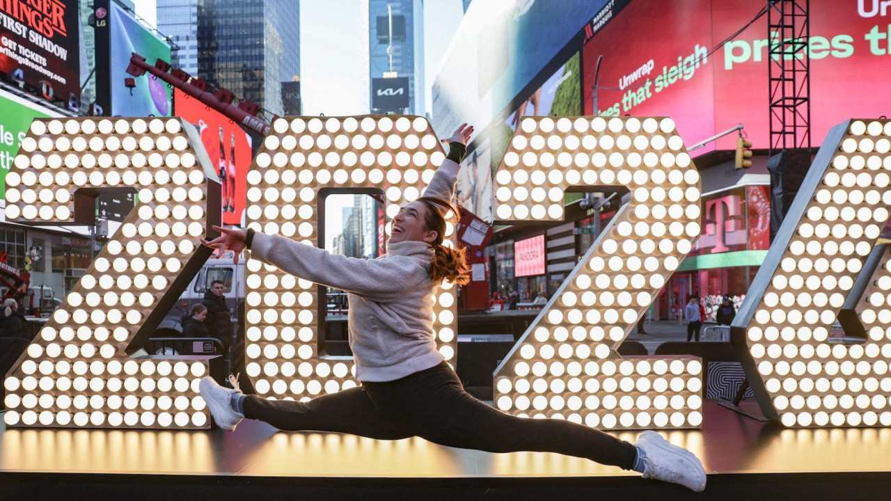 Devojka u trenerci skače ispred svetlećeg znaka na njujorškom Tajms Skveru