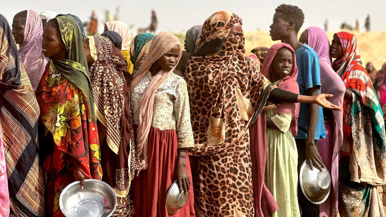Sudanke i Sudanci čekaju u redu za hranu, držeći metalne činije u rukama 