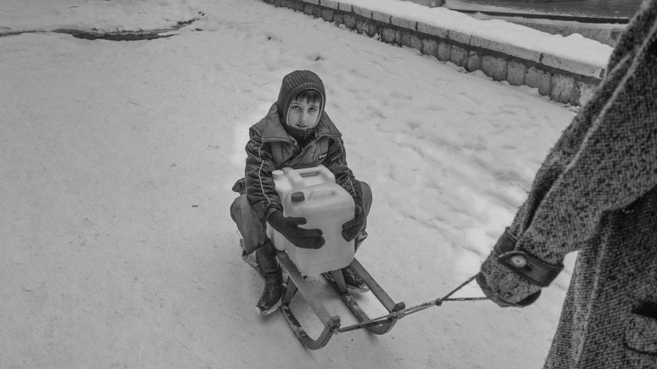 Dečak na sankama drži kanister sa vodom, crno-bela fotografija 