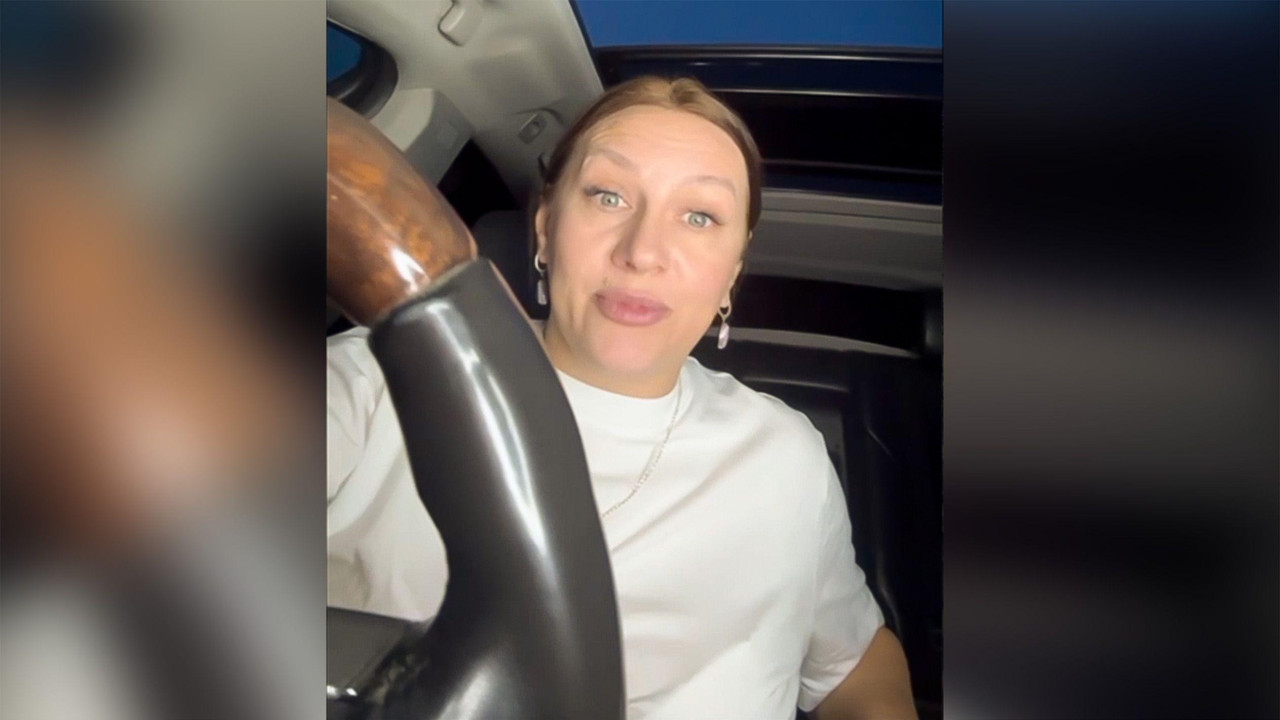 Polina Azarnik u beloj majici drži veliki volan, gledajući direktno u kameru. 