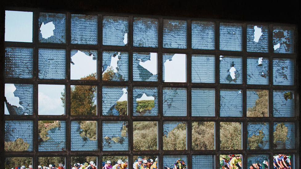 Kolona biciklista snimljena kroz okno delimično razbijenog prozora u napuštenoj zgradi tokom takmičenja u Španiji