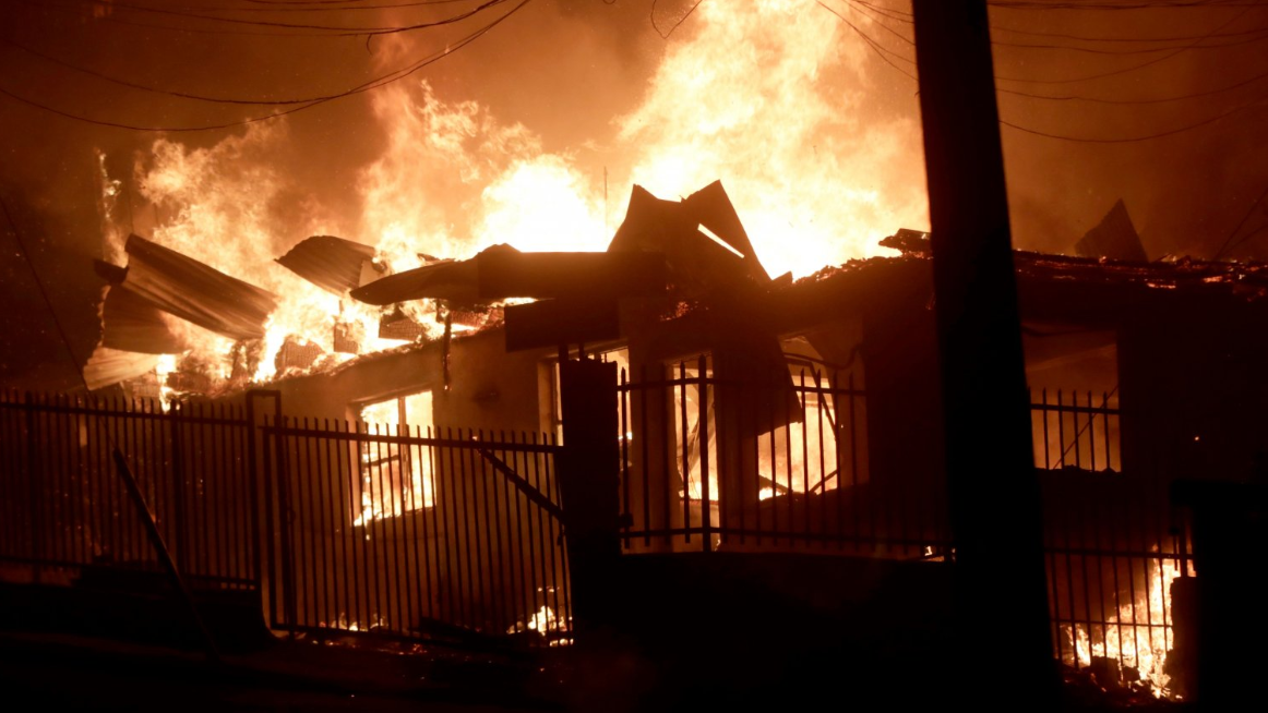 Houses affected by forest fires burn in Penco, Chile, 18 January 2026.