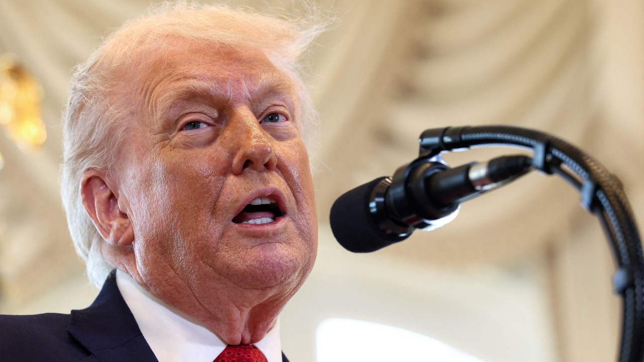 Krupna, talking head fotografija - Donald Tramp drži govor, ima crni sako, belu košulju i crvenu kravatu, pred njim je crni mikrofon, gleda u stranu