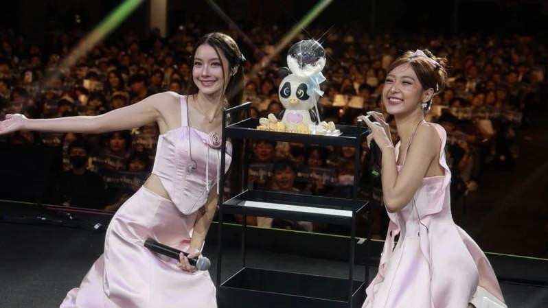 Dve devojke u rozim haljinama na sceni okrenute publici leđima