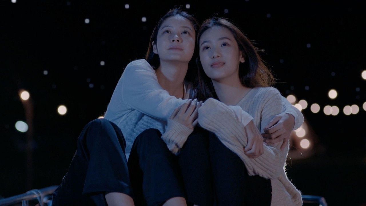 Dve devojke u belim džemperima se grle gledajući ka nebu