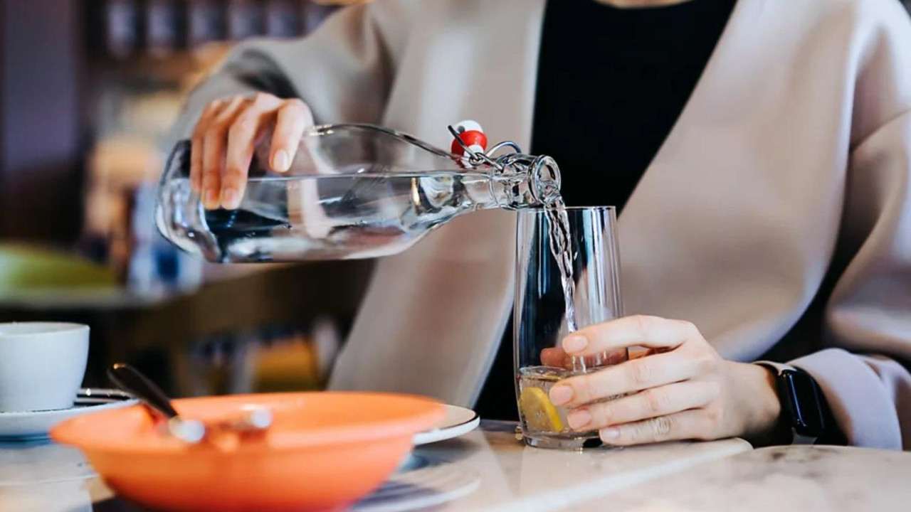 žena sedi za stolom i sipa vodu iz flaše u čašu