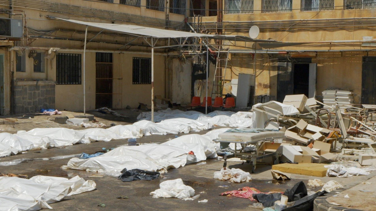 Bele plastične folije prekrivaju tela na parkingu bolnice u Suveidi. Ostaci polomljenih stolica i bolničkih kreveta takođe su razbacani po zemlji.