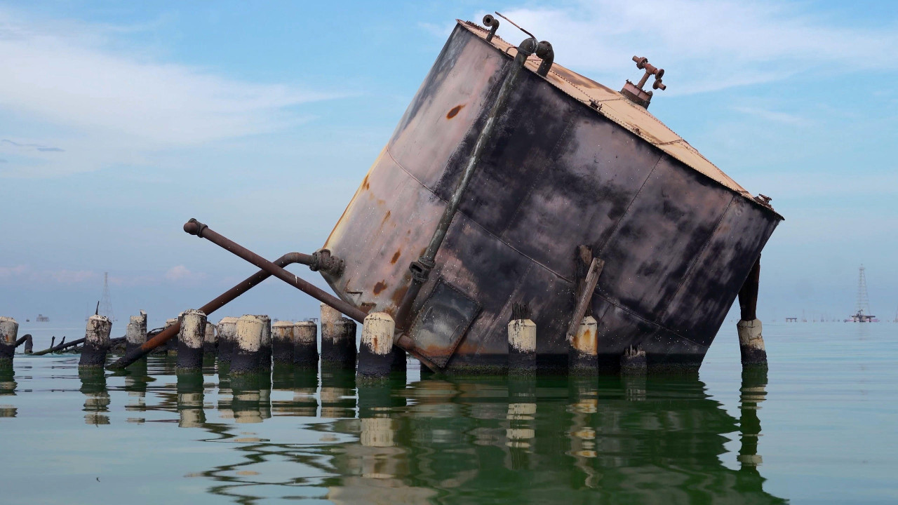 Napušteni, veliki, okrugli metalni rezervoar sa isturenim cevima nalazi se na nivou vode. Nagnut je tako da je deo osnove i bočne strane sa desne strane potopljen. Kratki, debeli stubovi sa prljavo belim vrhovima vire iz vode ispred rezervoara.
