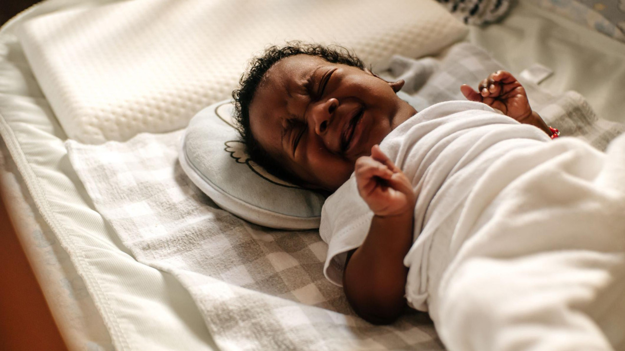 beba plače dok leži u krevecu i stiska pesnicu