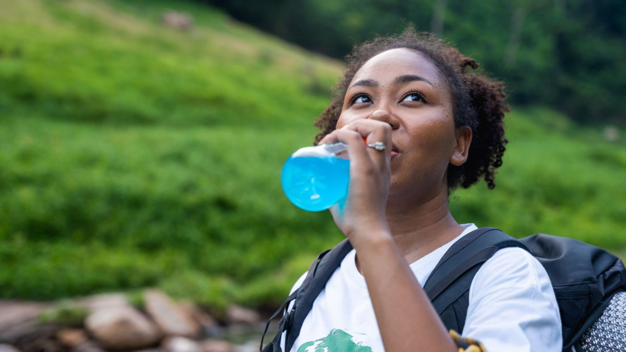 Devojka pije elektrolitski napitak u prirodi