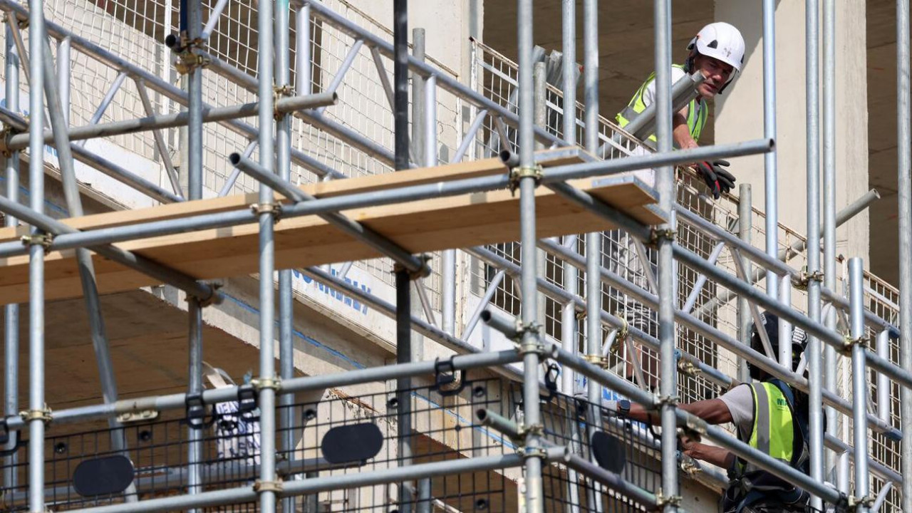 Građevinska skela i dva radnika u prslucima i sa kacigama na glavi