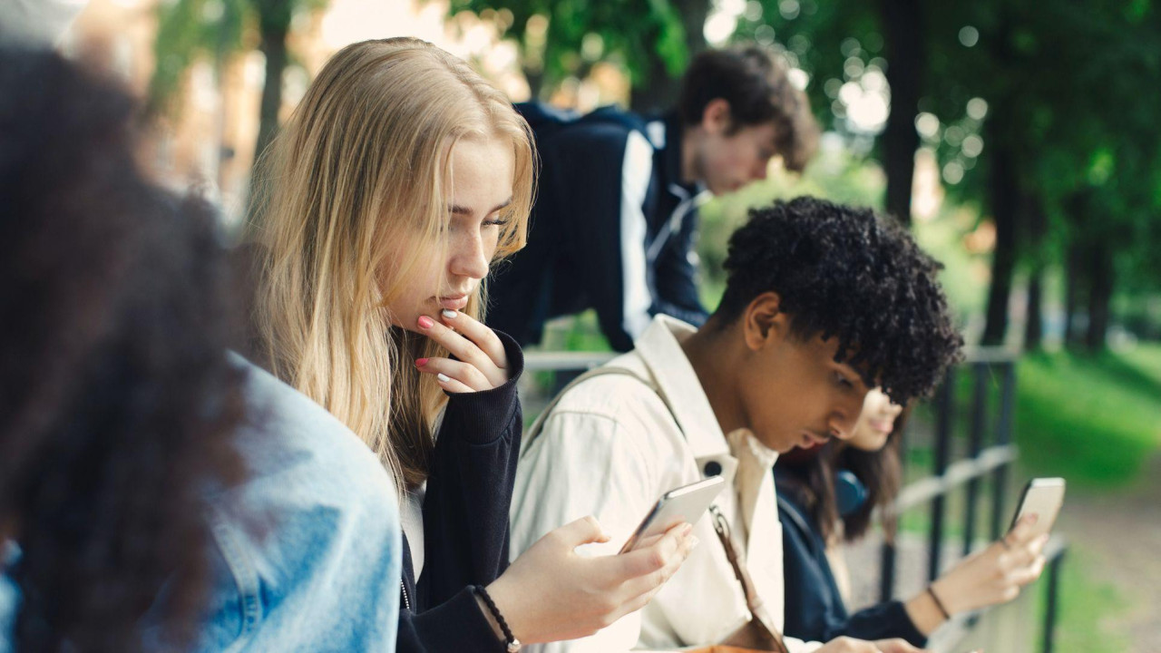 Stock image of three young people looking at their phones in a park.