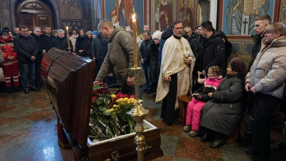 Čovek odaje počast nedavno žrtvi, sa otvorenim kovčegom sa cvećem usred crkvene sale i drugim ožalošćenim ljudima
