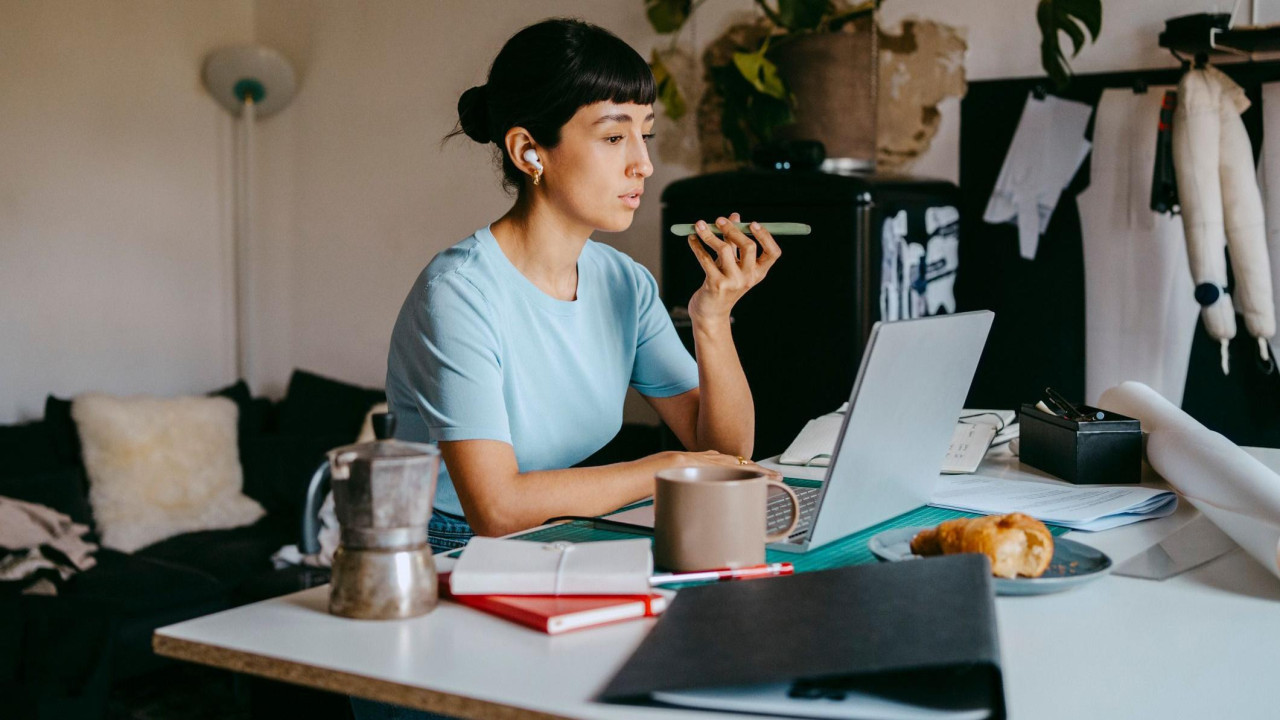 Devojka priča na telefon, ispred njen je laptop