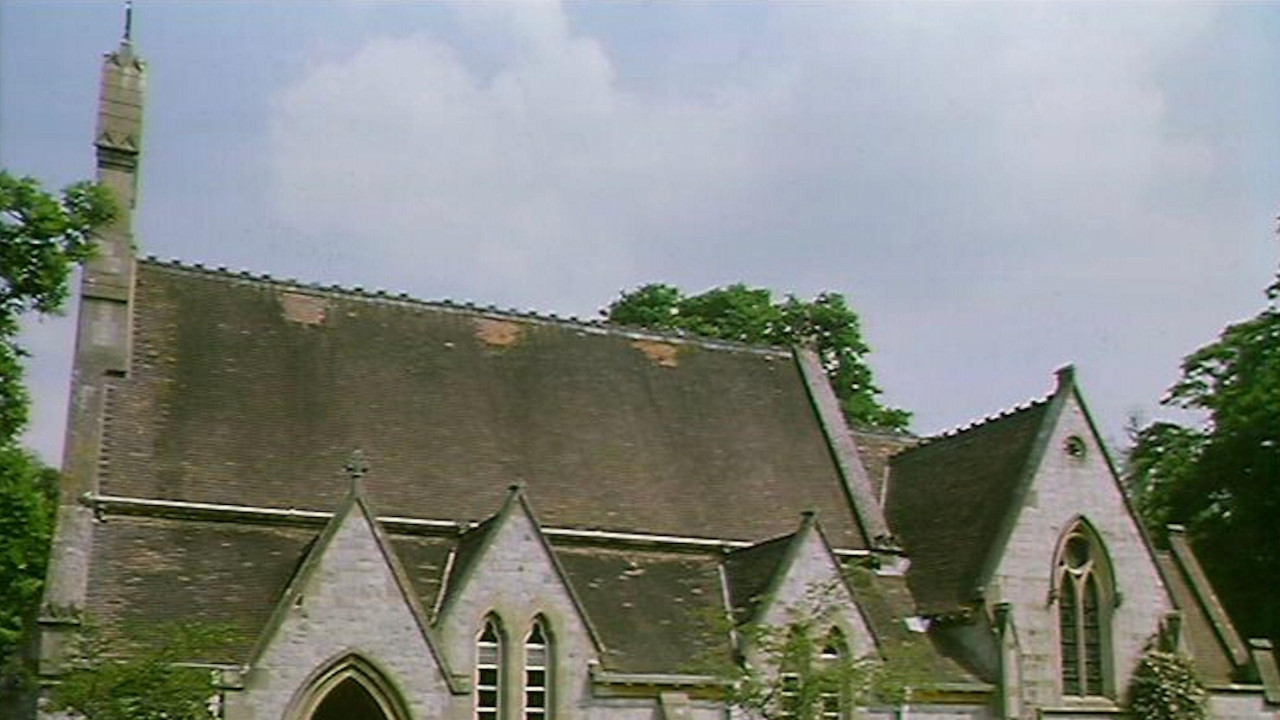 A chapel with a spire, pitched roof and arched entrance. A path and neat lawns are in front of it with small trees growing on the lawns.