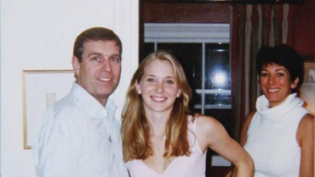 Andrew wearing a blue shirt with black trousers, standing next to Virginia Giuffre, with his arm around her waist. Ms Guiffre is wearing a tight tank top, revealing her lower stomach and multicoloured trousers with purple and pink patterns on them. Ghislaine Maxwell is standing behind them, leaning backwards a little. She is wearing a white top with a large circular collar that reveals her arms from her shoulders. All three are smiling.