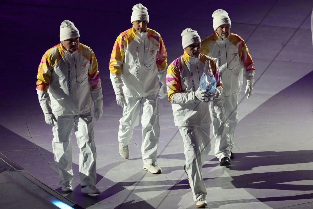 
                    Četvorica muškaraca u belim odelima i sa belim kapama na glavama, olimpijski šampioni iz Lilehamera 1994. godine, u štafeti 4x10 km u skijaškom trčanju, nose olimpijski p