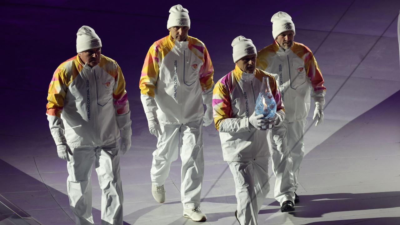 Četvorica muškaraca u belim odelima i sa belim kapama na glavama, olimpijski šampioni iz Lilehamera 1994. godine, u štafeti 4x10 km u skijaškom trčanju, nose olimpijski plamen