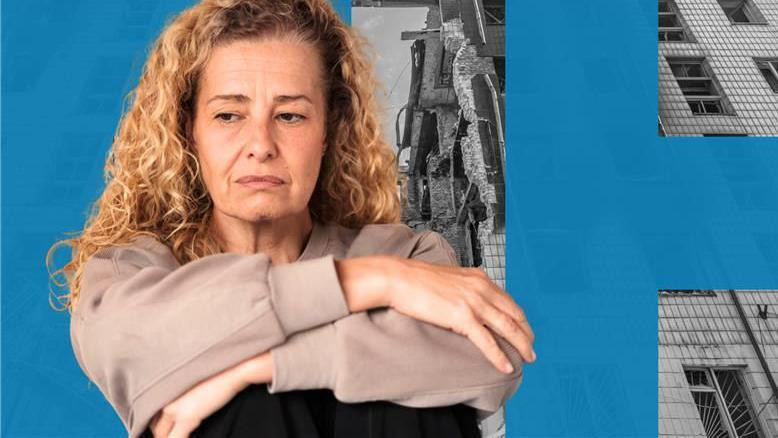 Žena sa dugom, plavom, kovrdžavom kosom, sedi sa rukama prekrštenim preko podignutih kolena. Ima zabrinut izraz lica. Nosi krem duksericu. U pozadini je crno-bela slika bombardovane zgrade.